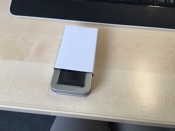 Metallbox mit Sichtfenster und weißer Kartonhülle auf Schreibtisch, Geschenkverpackung