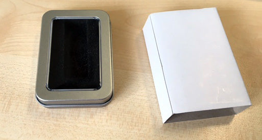 Metallbox für USB-Stick mit Sichtfenster und weißer Karton auf Holzoberfläche