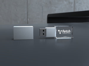 USB-Stick aus Kristallglas mit Metallkappe und Gravur, auf dunklem Tisch liegend