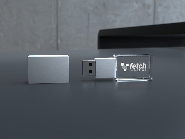 USB-Stick aus Kristallglas mit Metallkappe und Gravur, auf dunklem Tisch liegend